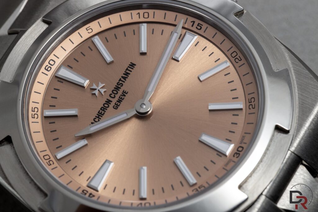 Macrofotografía del dial cepillado salmón de un Vacheron Constantin Overseas mostrando luz rasante y reflejos en cristal de zafiro.