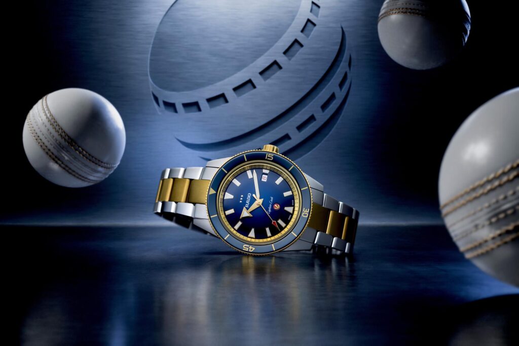 Reloj Rado Captain Cook European Cricket sobre fondo azul con pelotas de críquet