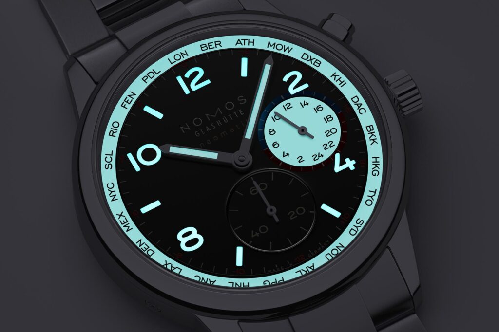 Vista nocturna del NOMOS Club Sport neomatik Worldtimer dark mostrando la luminiscencia Superluminova azul en el disco de ciudades y subesfera.