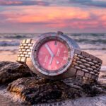 Reloj DOXA SUB 200T Afterglow edición limitada con esfera rosa inspirada en el atardecer sobre una superficie rocosa.
